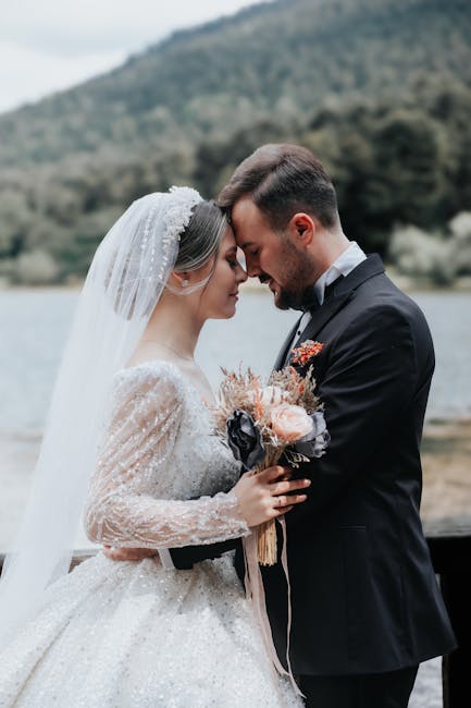 A couple in wedding attire sharing an intimate moment by a scenic lakeside.